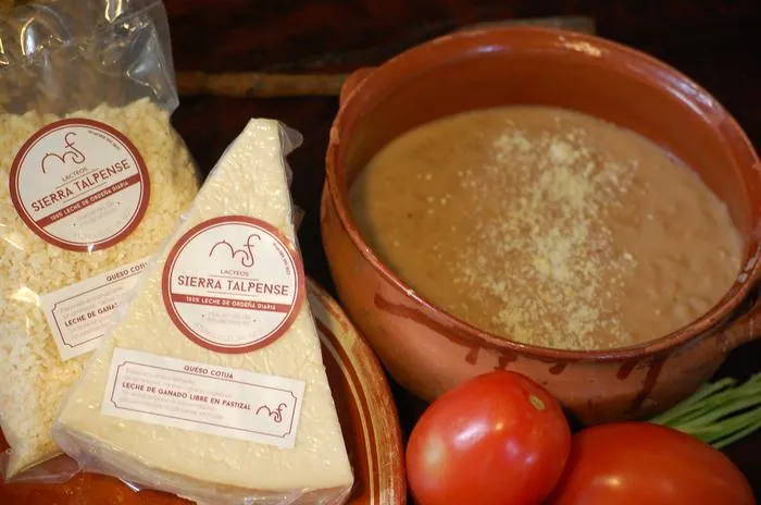Cotija rallado y en pieza junto a una olla de frijoles